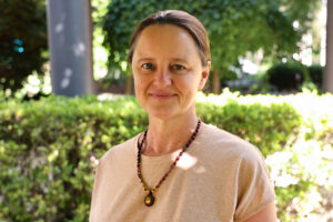 Woman standing in front of a bush smiling with a necklace on