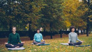 Three people meditating on yoga mats outside in a garden