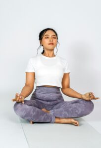 Lady sitting on a yoga mat meditating with a white background